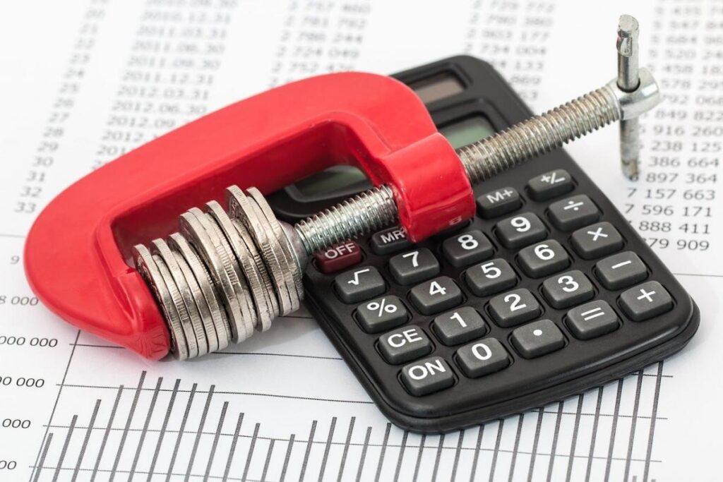 Calculator with a red clamp with coins clamped in it against a backdrop of financial statement