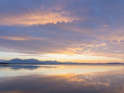 a pale sunset over a lake with mountains in the background