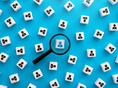 Magnifying glass focus on white square with blue figure in a group of white squares with black figure against a blue background.